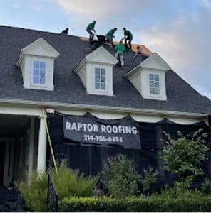 Two workers installing roofing on a house with a Raptor Roofing banner.